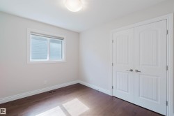 This room features rich, dark hardwood flooring, a window with horizontal blinds, and a pair of white paneled doors - 