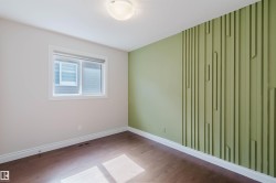 This room features hardwood flooring, a window providing natural light, and a distinctive green accent wall with a textured design - 