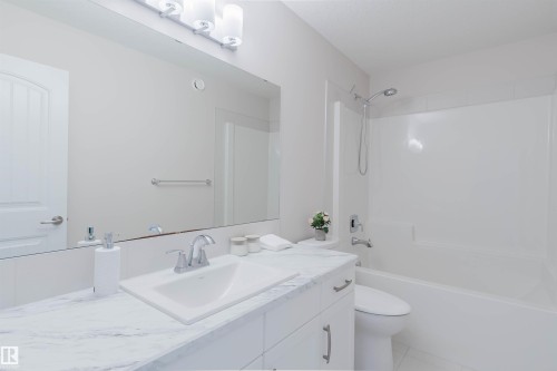 The bathroom features a vanity with a white countertop and a rectangular sink, a large mirror, and a bathtub with a shower - 4875 Wright Drive, Edmonton, AB - Indoor Photo Showing Bathroom