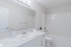 The bathroom features a vanity with a white countertop and a rectangular sink, a large mirror, and a bathtub with a shower - 