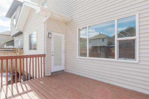 The property features a wooden deck with a matching railing, a glass-paned door, and large windows set into the light-colored siding - 4875 Wright Drive, Edmonton, AB - Outdoor With Deck Patio Veranda With Exterior