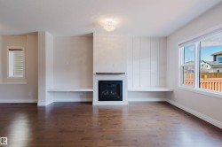 Spacious living area featuring rich hardwood floors, a fireplace with a wooden mantel, built-in shelving, and large windows providing natural light - 