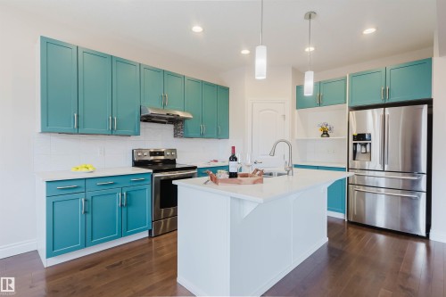 The kitchen features turquoise cabinetry, stainless steel appliances, a white tile backsplash, and a kitchen island with a sink and pendant lighting - 4875 Wright Drive, Edmonton, AB - Indoor Photo Showing Kitchen With Upgraded Kitchen