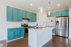 The kitchen features turquoise cabinetry, stainless steel appliances, a white tile backsplash, and a kitchen island with a sink and pendant lighting - 