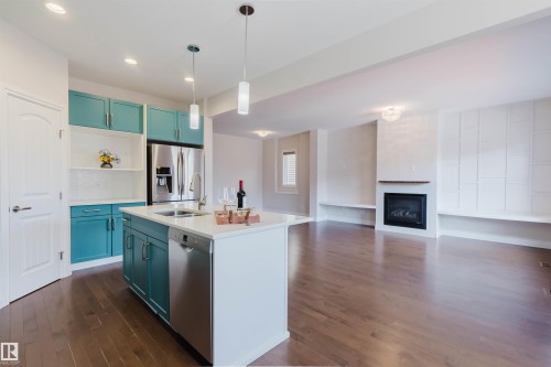 The open-plan living space features rich hardwood flooring, a modern kitchen with teal cabinetry, stainless steel appliances, and a central island with a sink - 4875 Wright Drive, Edmonton, AB - Indoor Photo Showing Kitchen With Fireplace With Double Sink With Upgraded Kitchen