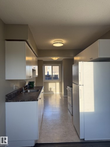 Kitchen featuring white cabinetry, dark countertops, a stainless steel sink, and tile flooring - 124 Cornell Court, Edmonton, AB - Indoor Photo Showing Kitchen With Double Sink