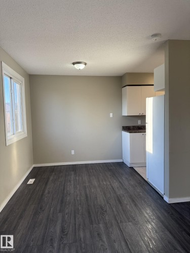 Bright room featuring dark wood-style flooring, a window, and a built-in kitchen area with white cabinetry and a white refrigerator - 124 Cornell Court, Edmonton, AB - Indoor Photo Showing Kitchen