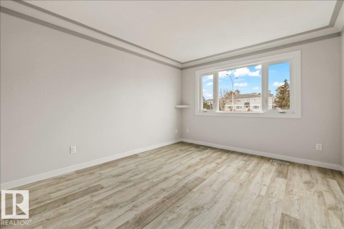 This spacious room features light-colored flooring, a large window with white trim, and a decorative ceiling trim - 12C Castle Terrace, Edmonton, AB - Indoor Photo Showing Other Room
