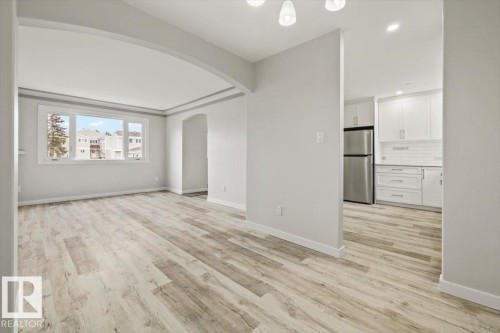 Expansive open concept living area featuring light-toned flooring, a large window, an arched entryway, and views towards the kitchen equipped with stainless steel appliances and white cabinetry - 12C Castle Terrace, Edmonton, AB - Indoor Photo Showing Other Room