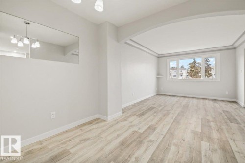 This living area features light-toned hardwood flooring, light grey walls, and a large window providing views of the exterior - 12C Castle Terrace, Edmonton, AB - Indoor Photo Showing Other Room