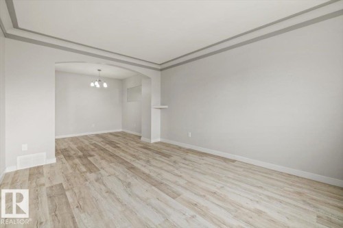 This inviting room features light-toned wood flooring and neutral-colored walls, complemented by a decorative ceiling trim - 12C Castle Terrace, Edmonton, AB - Indoor Photo Showing Other Room