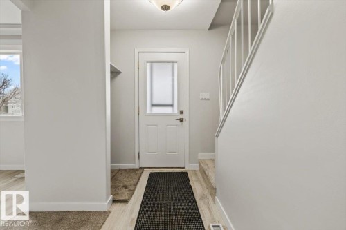 The entryway features light-toned flooring, white walls, a white door with a frosted glass insert, and a staircase with white railings - 12C Castle Terrace, Edmonton, AB - Indoor Photo Showing Other Room