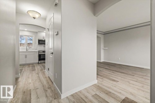 Inviting entrance featuring light-toned flooring, an arched doorway, and a view into the kitchen equipped with white cabinetry, a sink, and a window - 12C Castle Terrace, Edmonton, AB - Indoor Photo Showing Other Room