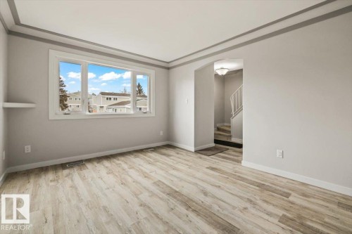 The property features light-colored walls, wood-style flooring, a large window, and an arched entryway - 12C Castle Terrace, Edmonton, AB - Indoor Photo Showing Other Room