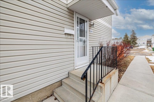 The property features neutral-toned siding, concrete steps with a black metal handrail, and a white storm door - 12C Castle Terrace, Edmonton, AB - Outdoor With Exterior