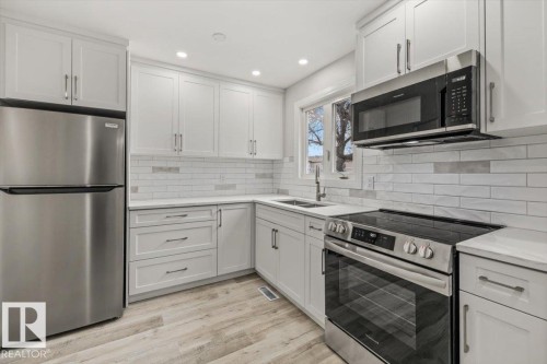 The kitchen features light-colored cabinetry, stainless steel appliances including a refrigerator, oven, and microwave, and a tiled backsplash - 12C Castle Terrace, Edmonton, AB - Indoor Photo Showing Kitchen With Double Sink With Upgraded Kitchen