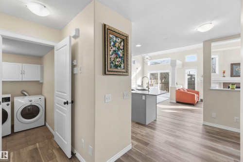 The property features light wood flooring, a laundry area with white appliances and wall-mounted cabinetry, and an open concept living space - 31 Everitt Drive, St. Albert, AB - Indoor Photo Showing Laundry Room