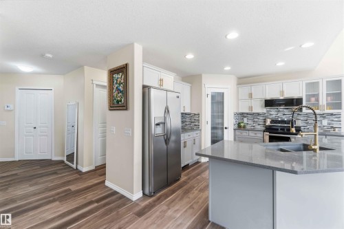 The kitchen features a large island with a sink and gold-toned faucet, stainless steel appliances, white cabinetry with gold-toned hardware, and a tiled backsplash - 31 Everitt Drive, St. Albert, AB - Indoor Photo Showing Kitchen With Upgraded Kitchen
