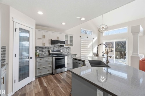 The kitchen features an island with a sink and faucet, stainless steel appliances, and wood-style flooring - 31 Everitt Drive, St. Albert, AB - Indoor Photo Showing Kitchen With Double Sink With Upgraded Kitchen
