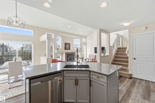 The open concept living area features a kitchen island with an integrated sink and dishwasher, hardwood floors, and a fireplace in the living room - 31 Everitt Drive, St. Albert, AB - Indoor Photo Showing Kitchen With Double Sink