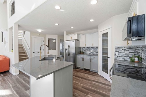 Modern kitchen featuring an island with a sink and a contemporary faucet, stainless steel appliances, a mosaic tile backsplash, and light-colored cabinetry - 31 Everitt Drive, St. Albert, AB - Indoor Photo Showing Kitchen With Upgraded Kitchen