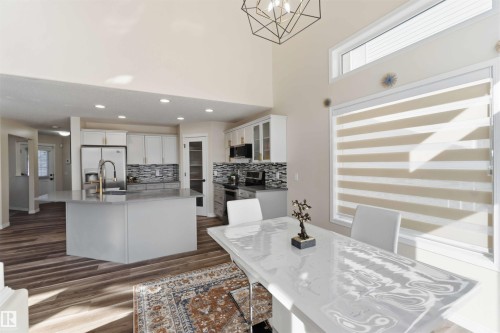 The kitchen features light-colored cabinetry, a spacious island with a sink, stainless steel appliances, and a tiled backsplash - 31 Everitt Drive, St. Albert, AB - Indoor