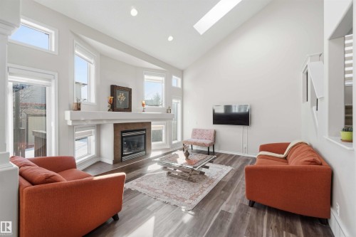 This living area features a high vaulted ceiling with a skylight, a fireplace with a stone surround, and large windows that provide ample natural light - 31 Everitt Drive, St. Albert, AB - Indoor Photo Showing Living Room With Fireplace