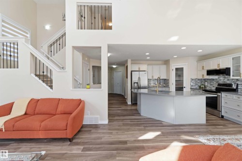 This open-concept living space features light wood-style flooring throughout, a kitchen with white cabinetry, a central island with a sink, and stainless steel appliances - 31 Everitt Drive, St. Albert, AB - Indoor Photo Showing Other Room