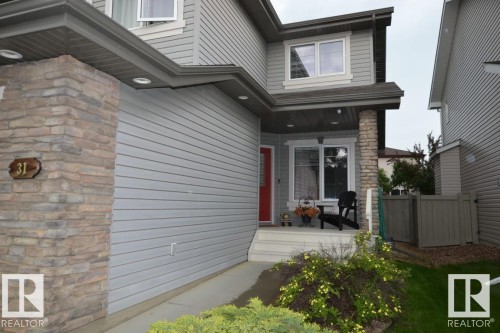 The property features a grey exterior with stone accents, a red front door, and a covered porch - 31 Everitt Drive, St. Albert, AB - Outdoor With Exterior
