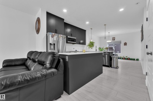 The open-concept living space features light-colored flooring, a kitchen with dark cabinetry, stainless steel appliances, and a central island with a light countertop - 1645 Plum Circle, Edmonton, AB - Indoor Photo Showing Kitchen With Upgraded Kitchen
