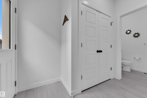 This space features light-colored flooring, white walls, a white paneled door with a window, and a white bi-fold door with dark hardware - 1645 Plum Circle, Edmonton, AB - Indoor Photo Showing Other Room