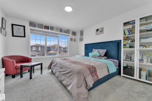 Well-lit interior space featuring a large window, light-colored carpeting, and a built-in shelving unit with glass doors - 1645 Plum Circle, Edmonton, AB - Indoor Photo Showing Bedroom