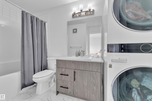 This bathroom features white tiled walls, a toilet, and a vanity with a rectangular sink, a white countertop, and dark-toned cabinetry - 1645 Plum Circle, Edmonton, AB - Indoor Photo Showing Laundry Room