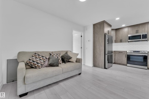 Living area featuring light-colored flooring and a kitchen with wood-look cabinetry, stainless steel appliances, and a white subway tile backsplash - 1645 Plum Circle, Edmonton, AB - Indoor Photo Showing Other Room