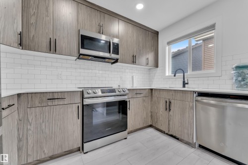 The kitchen features wood-look cabinetry, white subway tile backsplash, and a stainless steel appliance package, including a microwave, range, and dishwasher - 1645 Plum Circle, Edmonton, AB - Indoor Photo Showing Kitchen With Upgraded Kitchen