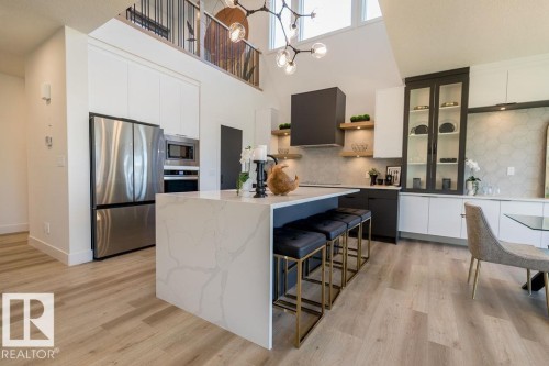 The kitchen features light wood flooring, a central island with a waterfall countertop, stainless steel appliances, and a modern chandelier - 102 Bluff Cove, Leduc, AB - Indoor Photo Showing Kitchen With Upgraded Kitchen