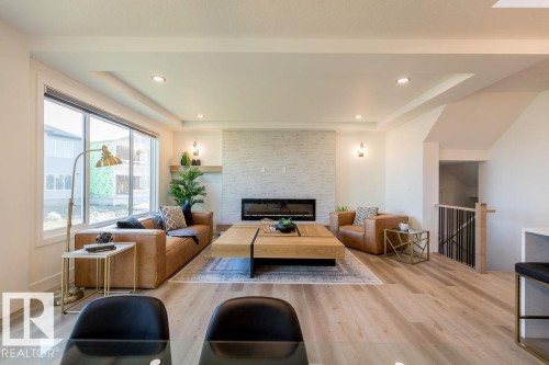 Bright living area featuring light-toned flooring, a fireplace with a textured surround, large windows, and recessed lighting - 102 Bluff Cove, Leduc, AB - Indoor Photo Showing Living Room With Fireplace