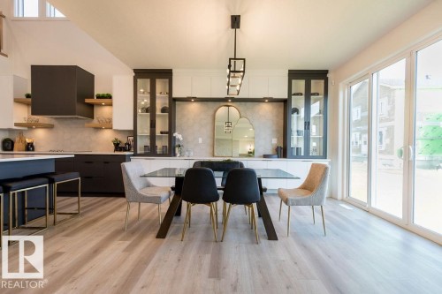 This open concept space features light-toned flooring, a modern kitchen with dark cabinetry and lighter countertops, and a dining area with a glass-top table - 102 Bluff Cove, Leduc, AB - Indoor