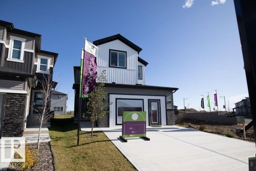 The property features a modern exterior with a white and gray facade, a concrete driveway, and a front yard with a tree and grass - 102 Bluff Cove, Leduc, AB - Outdoor