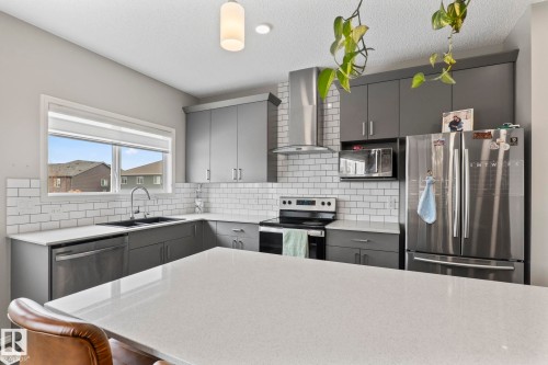 The kitchen features a large island with a light-colored countertop, dark grey cabinetry, a stainless steel refrigerator, and a window above the sink - 5164 Lark Crescent Nw, Edmonton, AB - Indoor Photo Showing Kitchen With Double Sink With Upgraded Kitchen