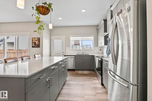 The kitchen features an expansive island with a light-colored countertop, gray cabinetry, and stainless steel appliances - 5164 Lark Crescent Nw, Edmonton, AB - Indoor Photo Showing Kitchen With Upgraded Kitchen