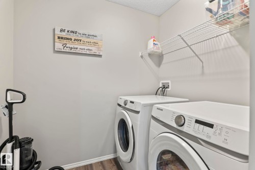 The property features a dedicated laundry area with white front-loading appliances, a wall-mounted wire shelf for storage, and wood-look flooring - 5164 Lark Crescent Nw, Edmonton, AB - Indoor Photo Showing Laundry Room
