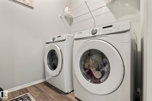 Dedicated laundry area featuring modern white front-loading appliances and a wire storage shelf - 5164 Lark Crescent Nw, Edmonton, AB - Indoor Photo Showing Laundry Room