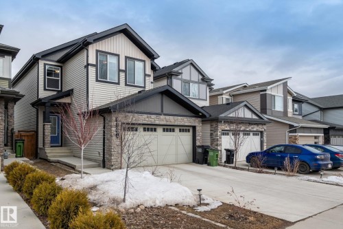 The property features light-colored horizontal siding with dark trim, a stone facade on the lower level, and an attached garage with a double door - 5164 Lark Crescent Nw, Edmonton, AB - Outdoor With Facade