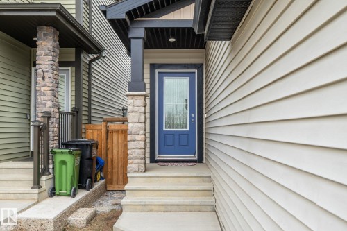 Property entrance featuring a blue door with a glass insert, flanked by stone-clad pillars, and concrete steps leading to the entrance - 5164 Lark Crescent Nw, Edmonton, AB - Outdoor