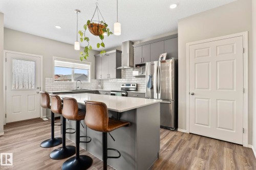 Kitchen featuring an island with seating, stainless steel appliances, grey cabinetry, and wood-style flooring - 5164 Lark Crescent Nw, Edmonton, AB - Indoor