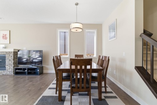 Open concept main floor with hardwood flooring, a stone-faced fireplace, and a dining area featuring a contemporary light fixture - 3235 Abbott Crescent, Edmonton, AB - Indoor Photo Showing Dining Room With Fireplace