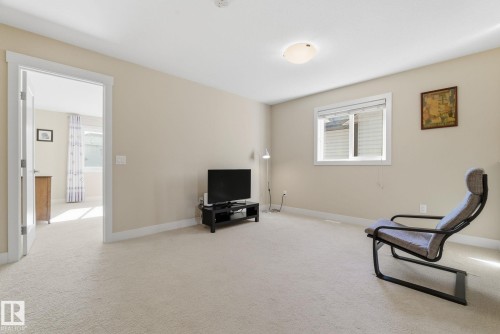 This inviting room features neutral-toned carpeting and walls, a window providing natural light, and a ceiling-mounted light fixture - 3235 Abbott Crescent, Edmonton, AB - Indoor