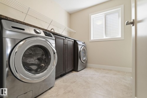 Laundry area featuring tile flooring, a window with blinds, dark wood cabinetry with a granite-style countertop, and wire shelving - 3235 Abbott Crescent, Edmonton, AB - Indoor Photo Showing Laundry Room