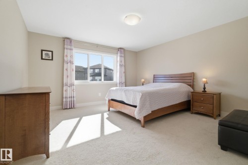 This spacious room features neutral-toned walls, light-colored carpeting, and a large window providing natural light - 3235 Abbott Crescent, Edmonton, AB - Indoor Photo Showing Bedroom